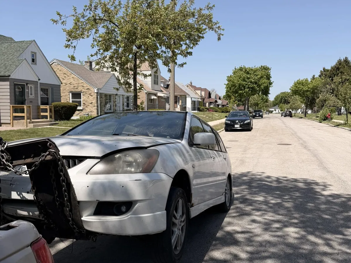 Damaged white sedan chained up for junk car pickup