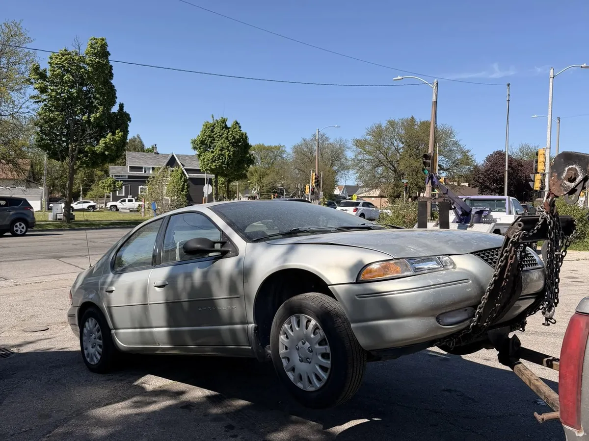 Silver sedan chained to a wheel lift for junk car pickup