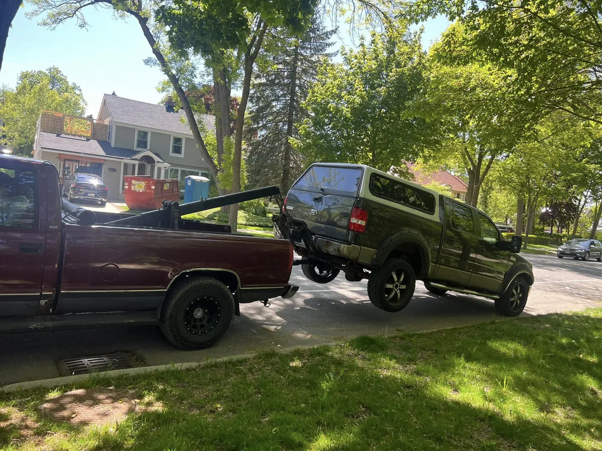 Maroon tow truck pulling a green pickup from a yard